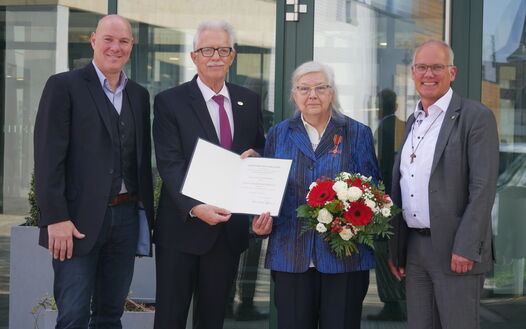 Elvira Enters-Krämer schaut mit Blumenstrauß und Urkunde in die Kamera. Neben ihr stehen drei Politiker, ganz links Bürgermeister Dirk Lukrafka. 